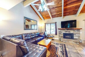 A living room with a leather sectional sofa, a flat-screen TV mounted above a stone fireplace, and a ceiling fan. - Modern condo with WiFi, fireplace, pool, & hot tub - near local attractions (Mammoth Lakes)
