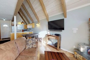Ein Wohnzimmer mit einer Couch, einem Couchtisch, einem Fernseher und einer Küchenzeile mit Esstisch.