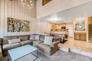 Ein modernes Wohnzimmer mit einem Ecksofa, einem Couchtisch und einem Essbereich, im Hintergrund ist eine Küche zu sehen.