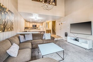 Ein Wohnzimmer mit Ecksofa, Couchtisch, Flachbildfernseher und einer Küche im Hintergrund.