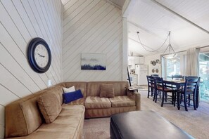 Ein Wohnzimmer mit braunem Ledersofa, einem Esstisch mit Stühlen, einer Uhr und einem Gemälde an der Wand.