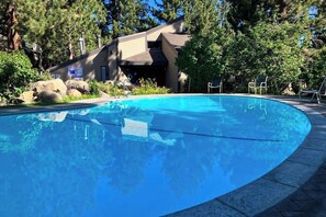 Ein klares, blaues Schwimmbecken, umgeben von Felsen und Bäumen, mit einem Gebäude im Hintergrund.