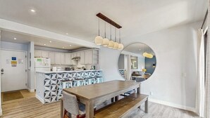 Een moderne keuken met witte kastjes, een centraal eiland en een eethoek met een houten tafel en bank.