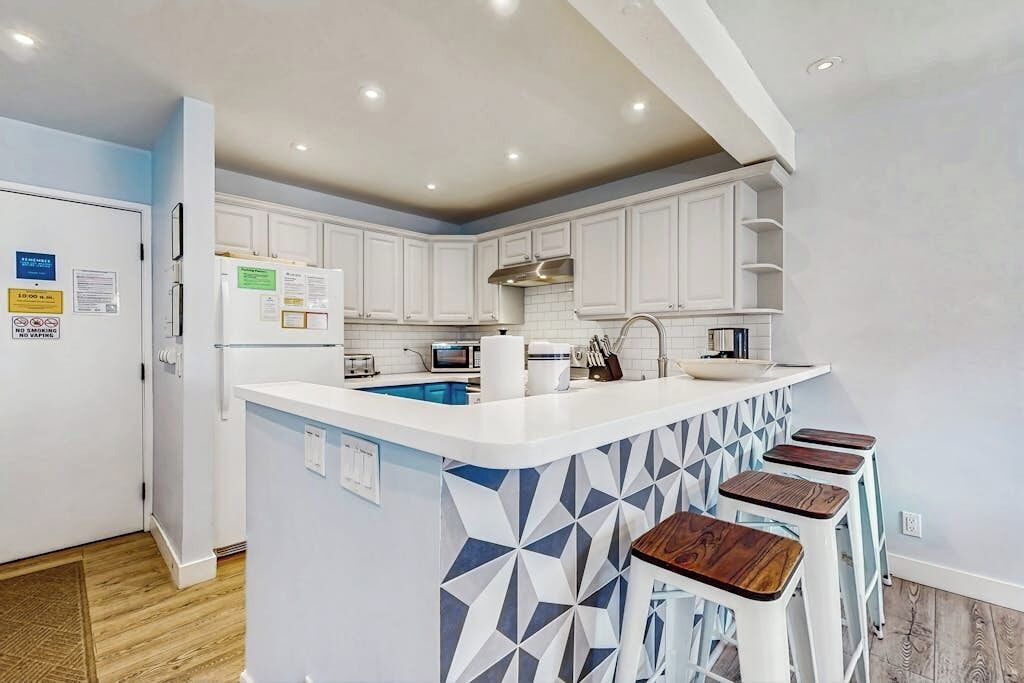 A modern kitchen with white cabinets, a central island with stools, and a microwave.