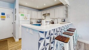 Een moderne keuken met witte kasten, een centraal eiland met krukken en een magnetron.