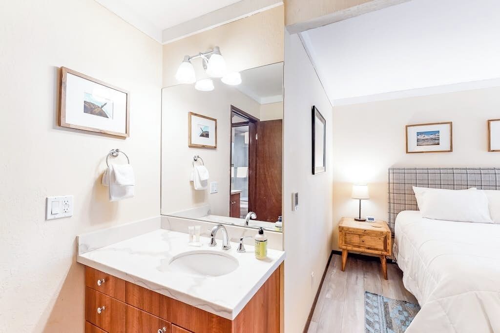 A hotel room with a bathroom, a bed, a bedside table, and a nightstand.