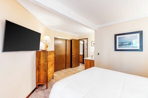 Ein Hotelzimmer mit einem Bett, einer Holzkommode, einem Fernseher, einem Schreibtisch mit Lampe und einem gerahmten Bild an der Wand.