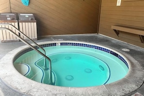 Ein Whirlpool mit Metallleiter, einer Fliesenleiste und einer Holzwand im Hintergrund.