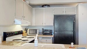 A kitchen with white cabinets, a black refrigerator, a microwave, a toaster, and a stove. - Comfy Condo Close to Skiing with Fireplace, Seasonal Pool, Hot Tub, & WiFi (Mammoth Lakes)