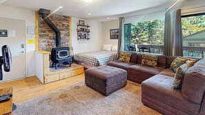 A cozy living room with a fireplace, a sofa, and a large window offering a view. - Comfy Condo Close to Skiing with Fireplace, Seasonal Pool, Hot Tub, & WiFi (Mammoth Lakes)