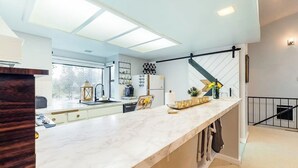 A modern kitchen with a marble countertop, a hanging light fixture, and a staircase with a black railing. - Marvelous & elegant two-story condo w/mtn views, private hot tub, gas fireplace (Mammoth Lakes)