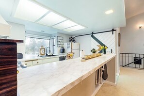 Eine moderne Küche mit Marmorarbeitsplatte, einer Hängeleuchte und einer Treppe mit schwarzer Handläufung.