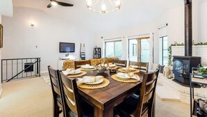 A dining area with a wooden table set for four, a chandelier, a ceiling fan, and a fireplace. - Marvelous & elegant two-story condo w/mtn views, private hot tub, gas fireplace (Mammoth Lakes)