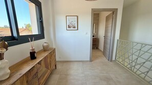 Un pasillo con una consola de madera, un cuadro en la pared y vistas al exterior a través de una ventana.