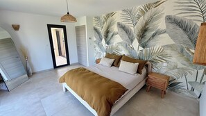 Un dormitorio con una cama, una lámpara colgante, una puerta y una pared con diseño de hojas.