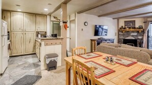 Eine Küche mit Holzausstattung, einem Esstisch mit Unterlagen, einem Sofa, einem Fernseher und einem Kamin.