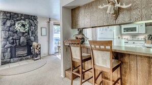 Une cuisine avec un mur en pierre, un plafond en bois, une cheminée en pierre et un îlot central avec des chaises.