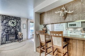 A kitchen with a stone wall, a wooden ceiling, a stone fireplace, and a kitchen island with chairs. - Comfy corner condo w/ shared, seasonal pool, hot tub, & rec room (Mammoth Lakes)