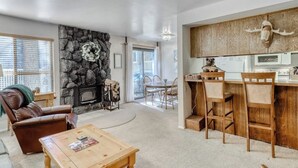 Un salon avec une cheminée, un coin repas et une cuisine dotée de meubles en bois et décorée d’un crâne d’ours.