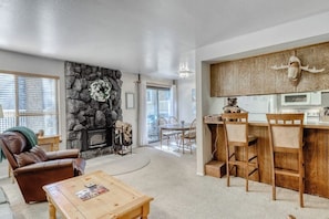 A living room with a fireplace, a dining area, and a kitchen with wooden cabinets and a bear skull decoration. - Comfy corner condo w/ shared, seasonal pool, hot tub, & rec room (Mammoth Lakes)