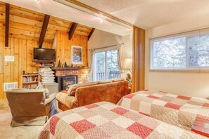 Ein gemütliches Zimmer mit Kamin, Fernseher, Bett und Fenster mit Blick auf Bäume.