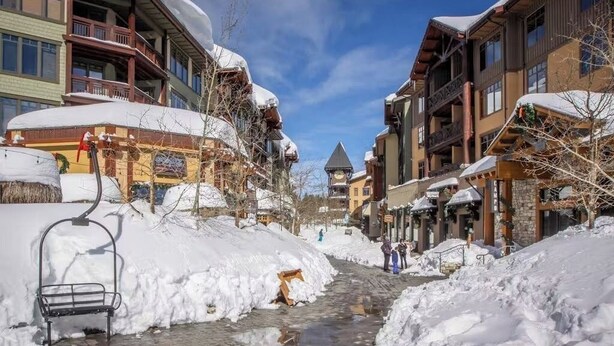 A snow-covered street with buildings, a bench, and a ski lift. - Updated condo w/ shared Pools, Hot Tubs, Saunas, Fitness Room & Tennis Courts (Mammoth Lakes)