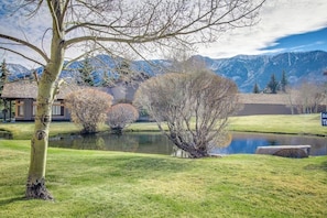 Eine friedliche Landschaft mit Teich, Bäumen und Bergen im Hintergrund.