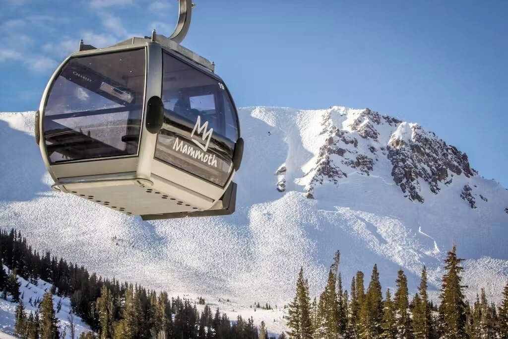 Una funivia con marchio 'Mammoth', sospesa sopra un paesaggio montano innevato.