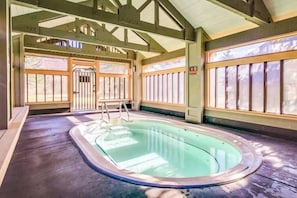 Ein Hallenbad mit einer Leiter, Holzbalken und großen Fenstern.