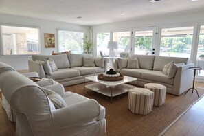 A modern living room with a beige sofa set, a coffee table, and striped ottomans. - Docktails and Daydreams lake LBJ bungalow sleeps 13 (Burnet)