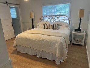 Ein Schlafzimmer mit einem Bett, zwei Nachttischen, einem Fenster mit Jalousien und einer Tür.
