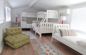 Um quarto com beliches, um sofá verde, uma mesinha com luminária e um tapete estampado.