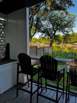 A covered outdoor seating area with chairs and a table, overlooking a water body and greenery. - Docktails and Daydreams lake LBJ bungalow sleeps 13 (Burnet)