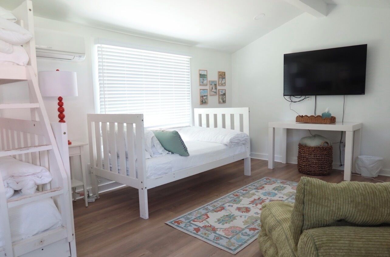 A child's room with a bunk bed, a single bed, a television, and a small table.