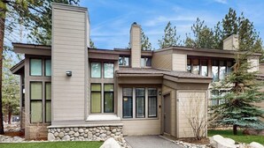 Une maison moderne à deux étages, dotée de fondations en pierre, de grandes fenêtres et d’un chemin en pierre menant à l’entrée.
