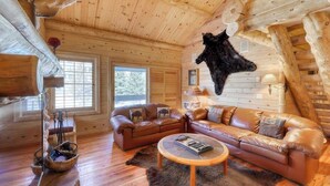 A log cabin interior with a leather sofa, a coffee table, and a mounted animal hide. - Luxurious condo with a fireplace & shared washer/dryer, pool, hot tub, & sauna (Mammoth Lakes)