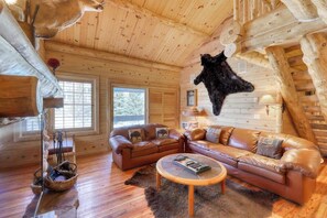 Ein rustikales Blockhaus-Interieur mit Ledersofa, Couchtisch und einem aufgehängten Tierfell.