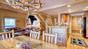 A log cabin interior with a dining area, a fireplace, and a kitchen. - Luxurious condo with a fireplace & shared washer/dryer, pool, hot tub, & sauna (Mammoth Lakes)