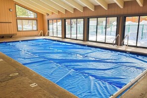 En indendørs swimmingpool med glasvægge, metalstiger og træbeklædning.