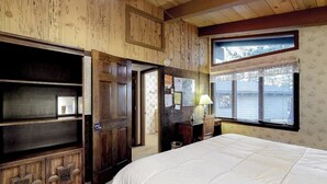 Ein Zimmer mit Holzwänden, einem Bett, einem Schreibtisch und einem Fenster mit Jalousien.