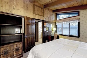 Ein Zimmer mit Holzwänden, einem Bett, einem Schreibtisch und einem Fenster mit Jalousien.