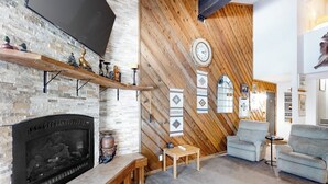 A living room with a fireplace, wooden wall paneling, a clock, and a sofa.