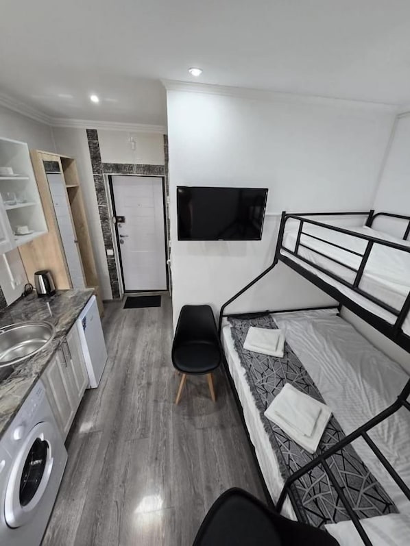 A compact room with a bunk bed, a washing machine, a flat-screen TV, and a small seating area.