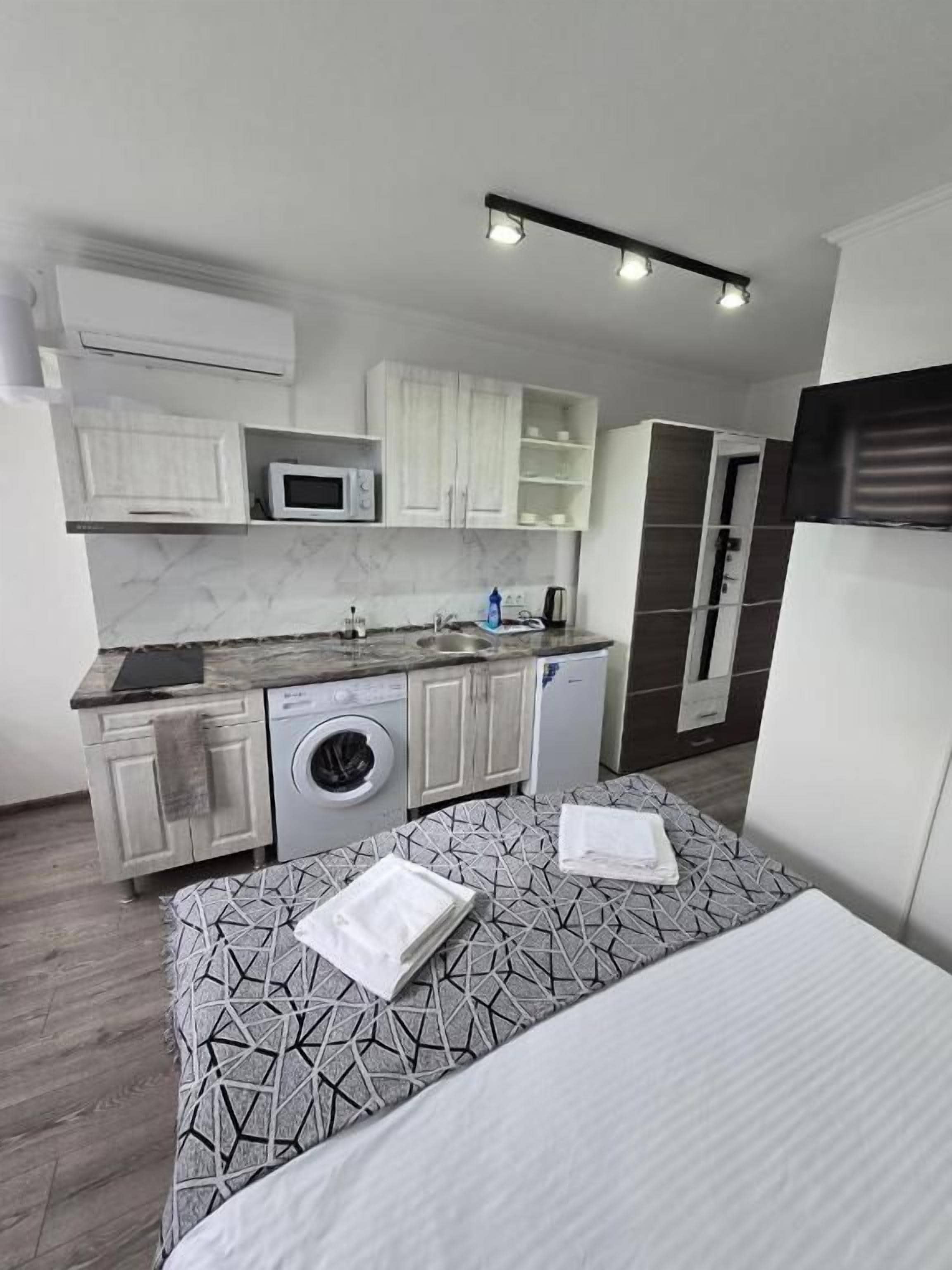 Una habitación de hotel compacta con cama, kitchenette pequeña, lavadora y microondas.
