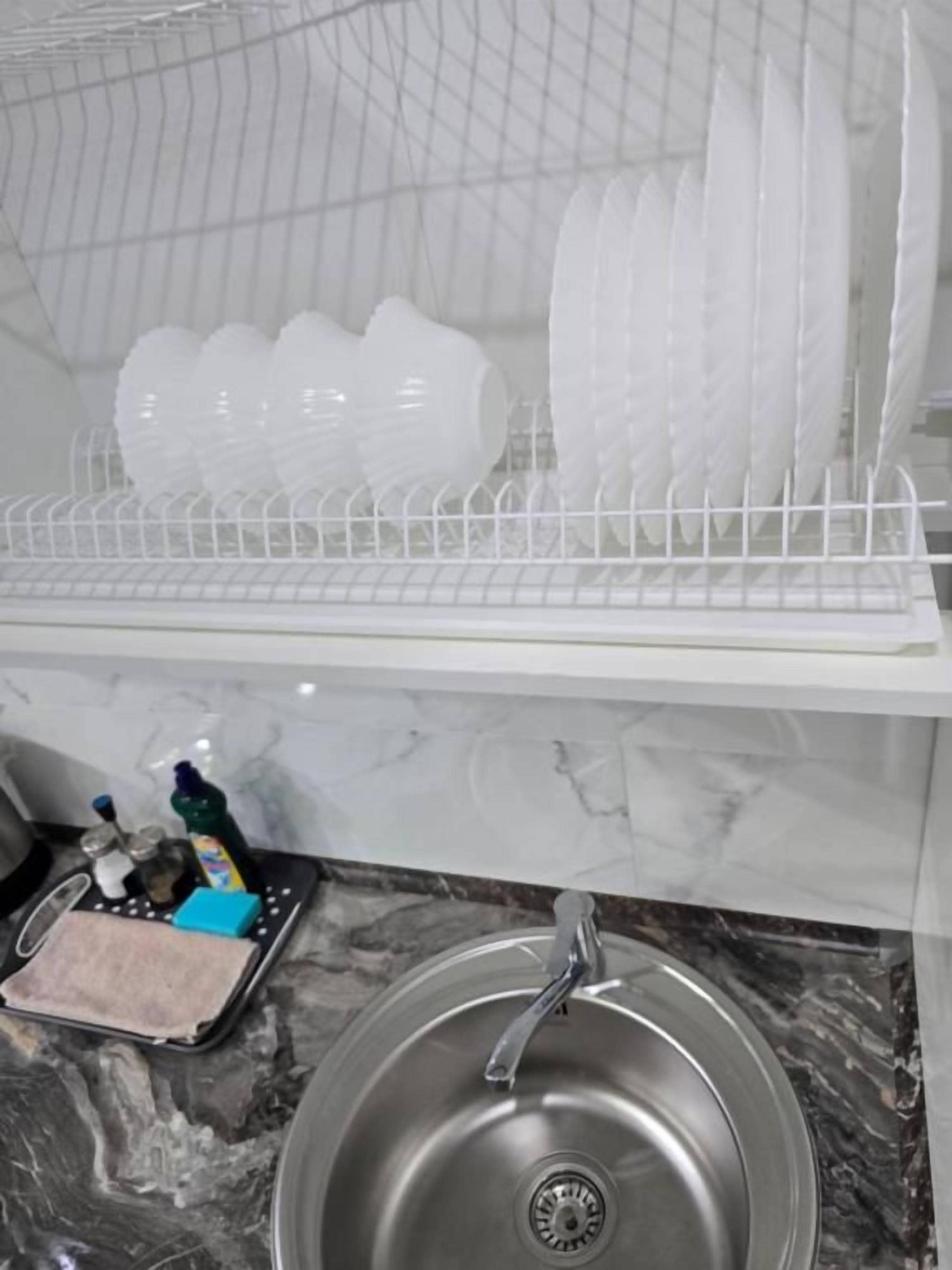Una cocina con un lavamanos de acero inoxidable, un escurreplatos con vajilla blanca y una encimera de mármol.