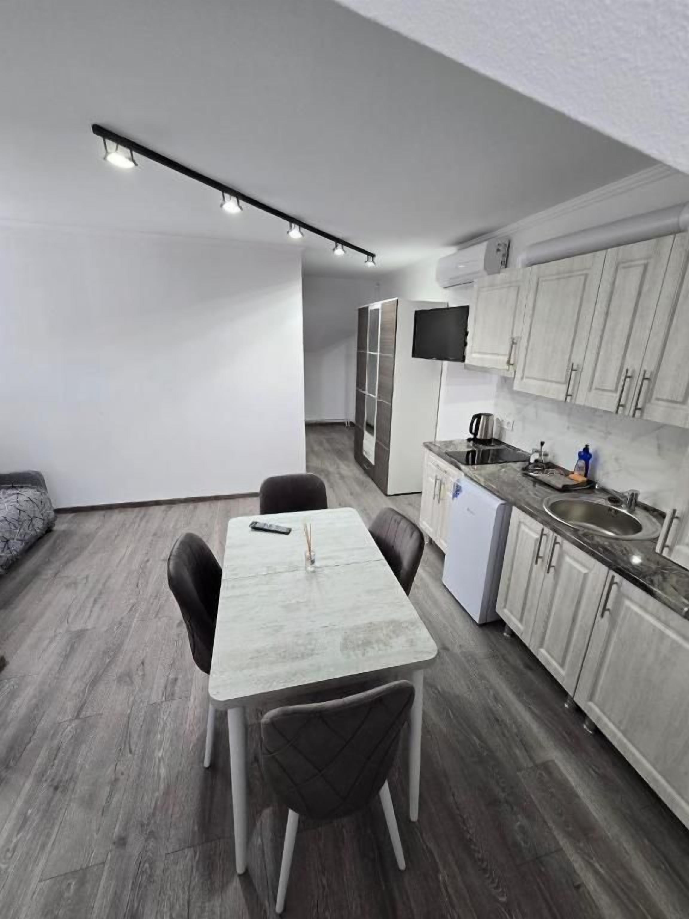 A compact kitchen with a dining area, white cabinets, a built-in oven, and a flat-screen TV.