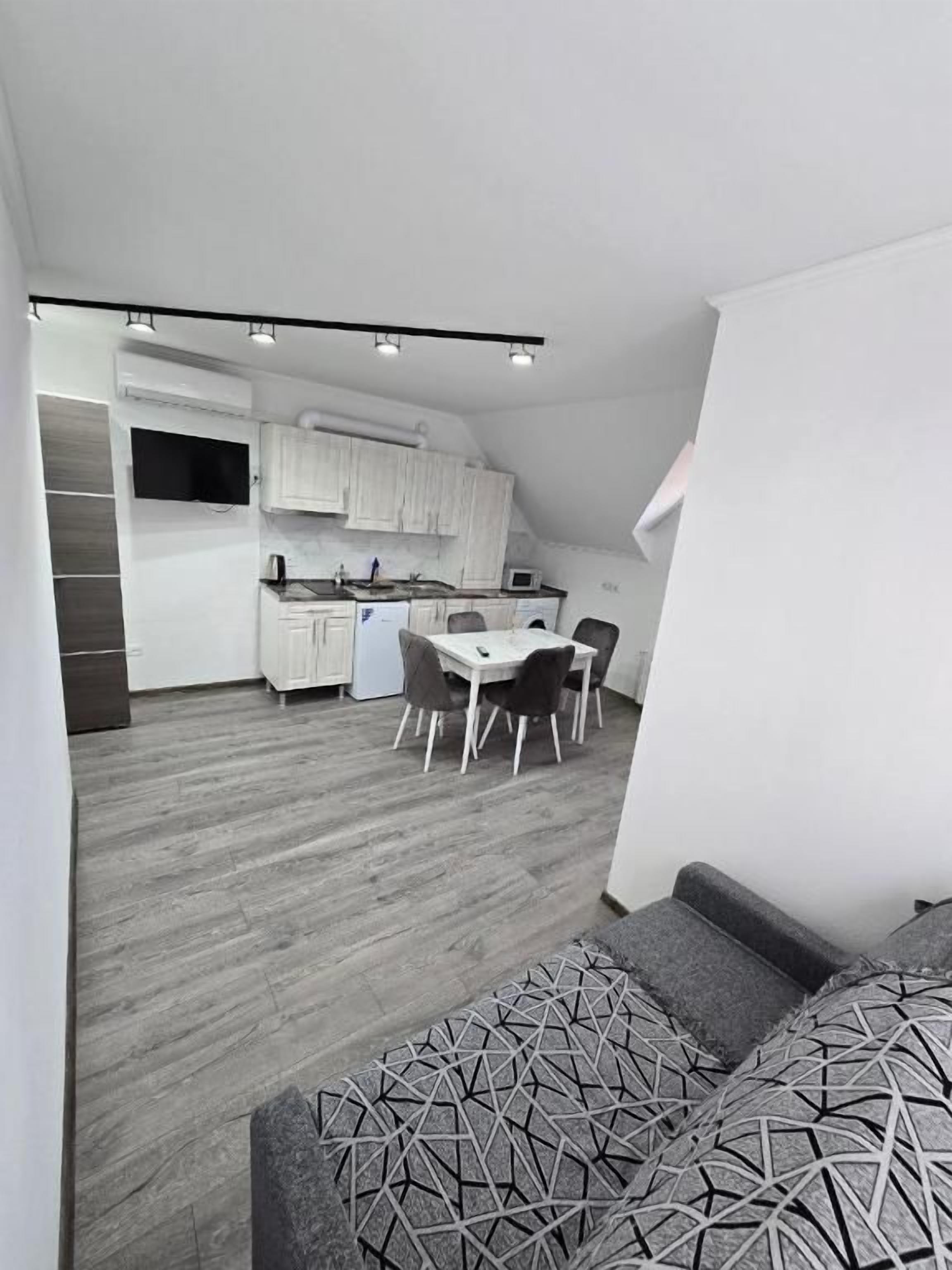 Una cocina moderna con armarios blancos, un comedor con mesa y sillas, y un sofá gris con estampado.