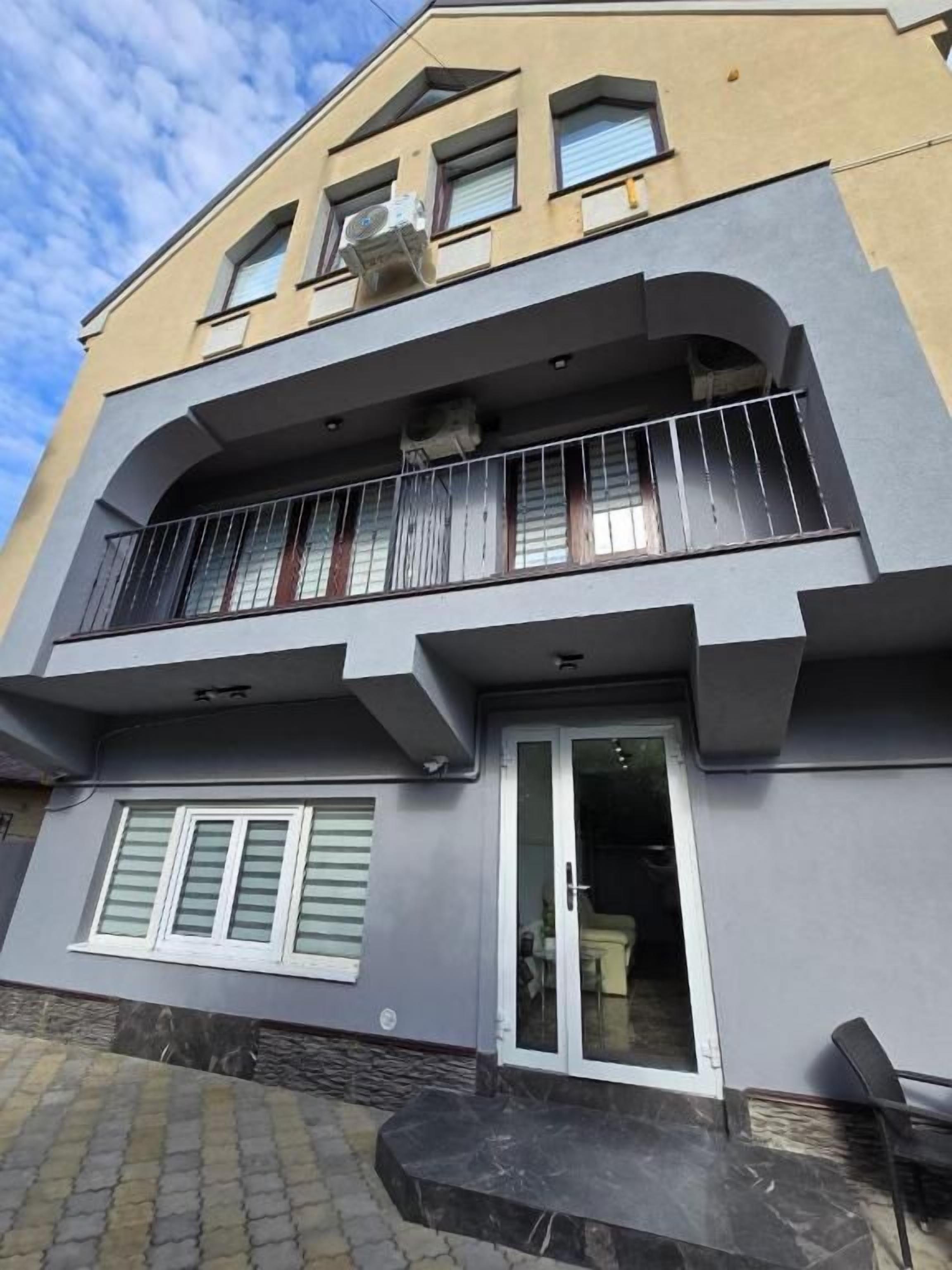 Un edificio de dos pisos con un balcón, una puerta con paneles de vidrio y una ventana con contraventanas.