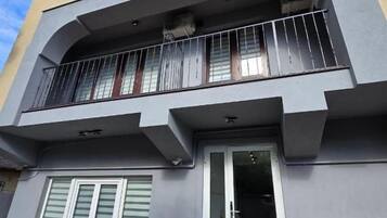 A two-story building with a balcony, a door with glass panels, and a window with shutters.