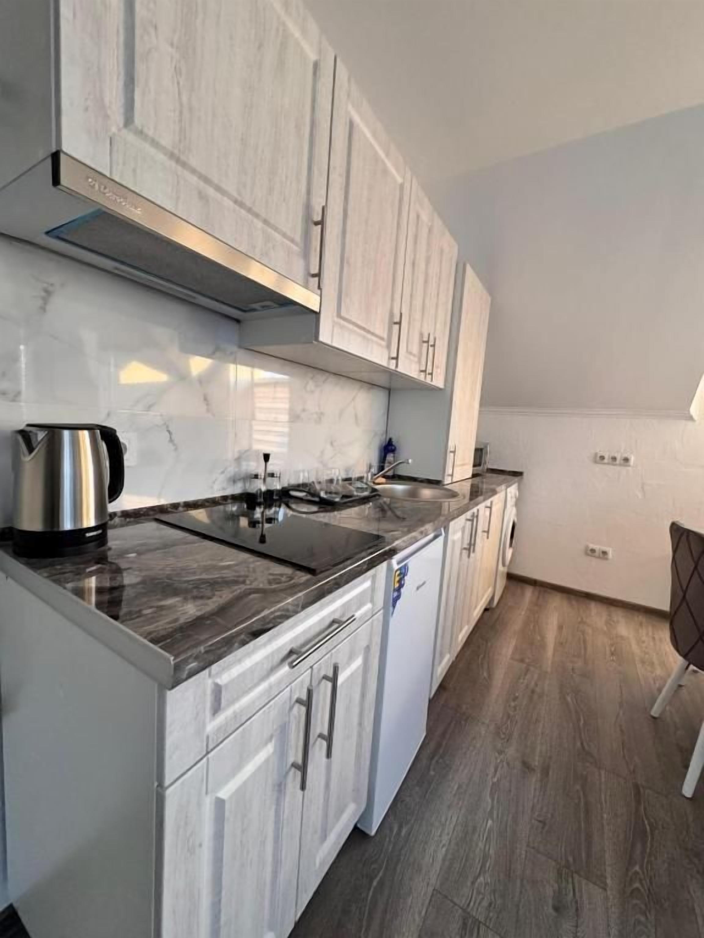 A kitchen with white cabinets, a black countertop, and a stainless steel kettle.
